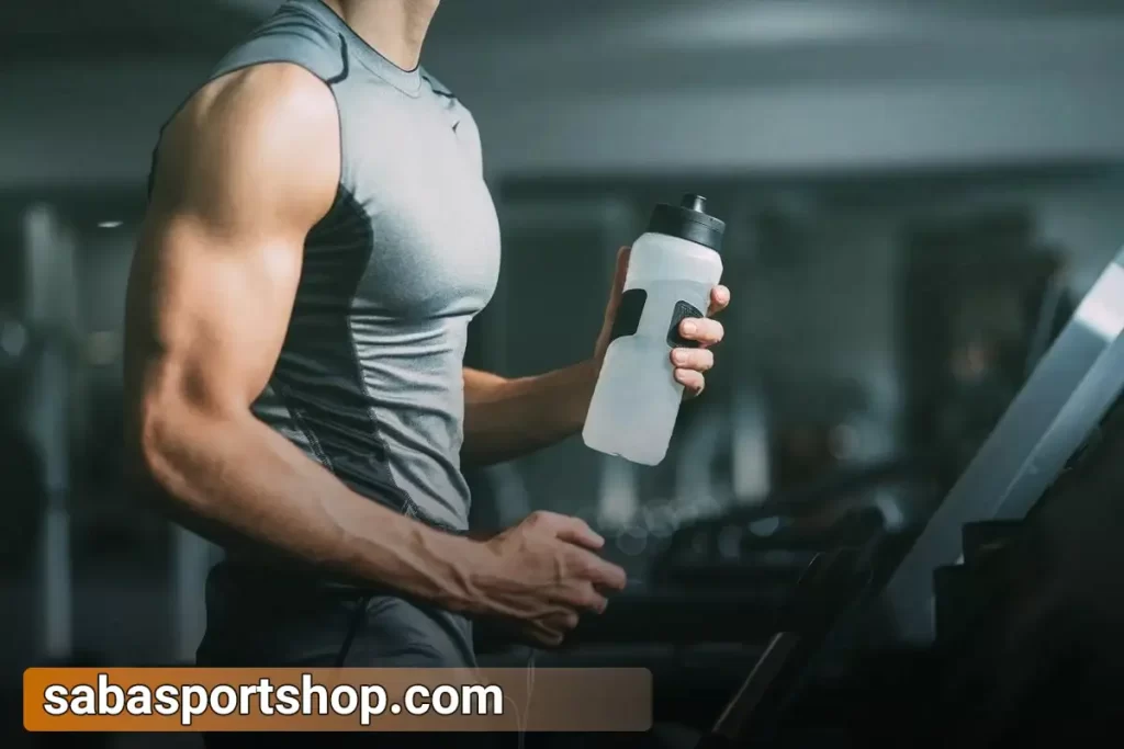 یک ورزشکار مرد در حال دویدن روی تردمیبل و آب خوردن